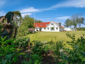 A white house with a red roof, surrounded by a well-maintained lawn and garden. - 5 Star Holiday Home in Lokken (Lokken)