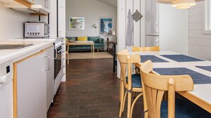 Een compacte keuken met witte kastjes, een magnetron en een spoelbak. Een eethoek met een tafel en stoelen is te zien, met een blauwe placemat.