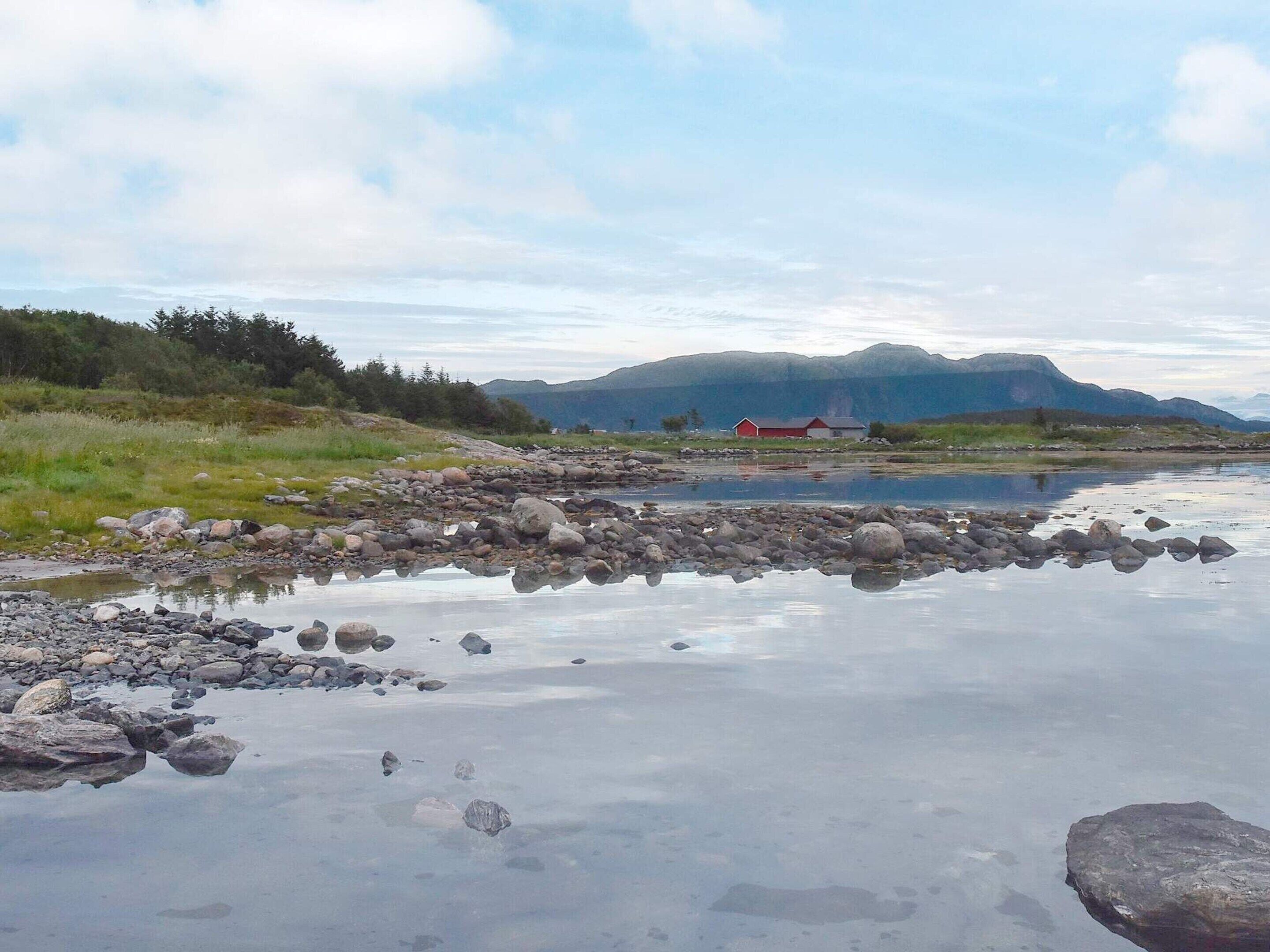 A calm river with rocks and a red building in the distance.
