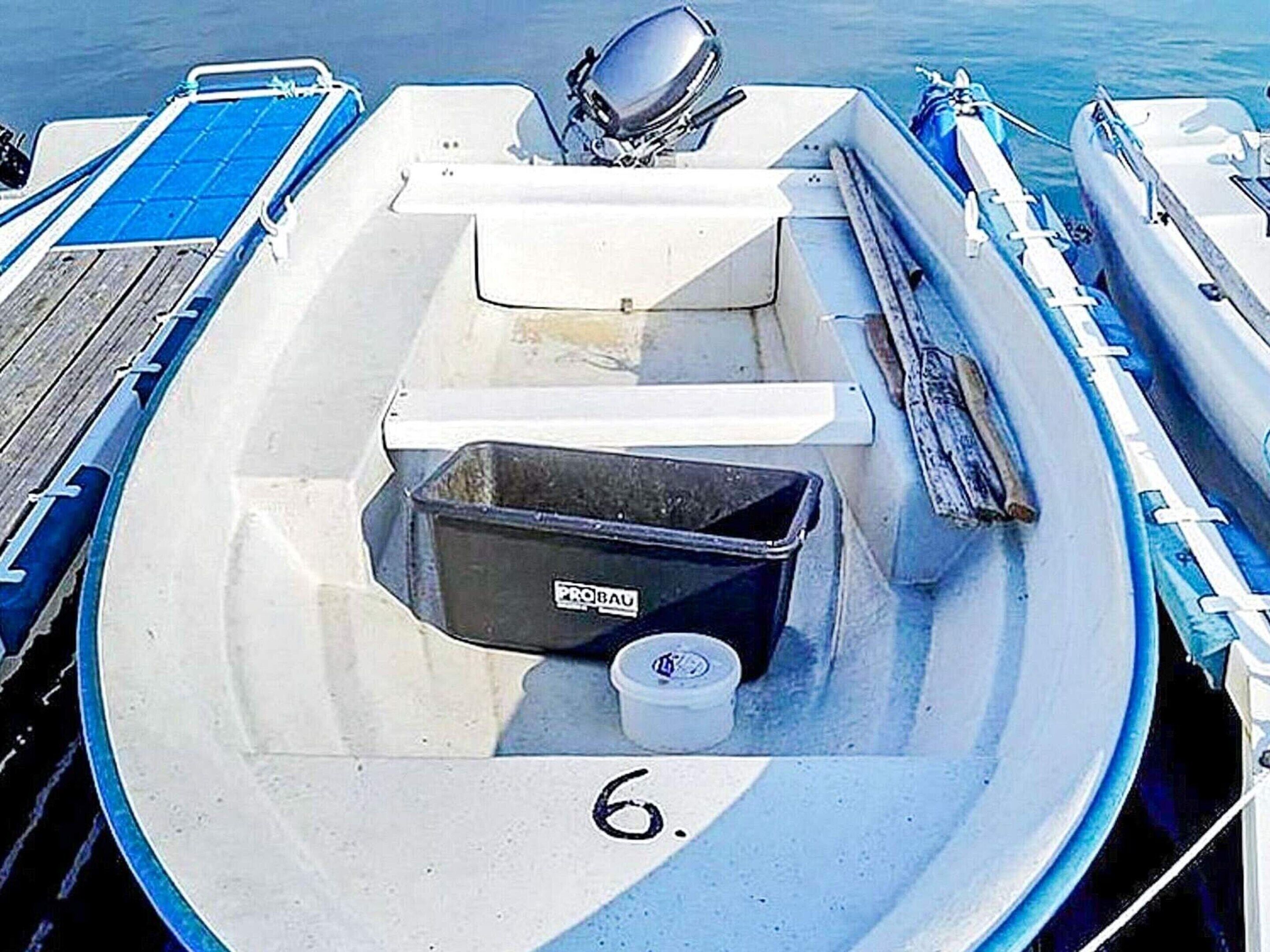 Ein kleines Boot mit weißem Innenraum, einer schwarzen Aufbewahrungsbox mit der Aufschrift "PROBAU" und der Zahl "6" auf dem Boden.