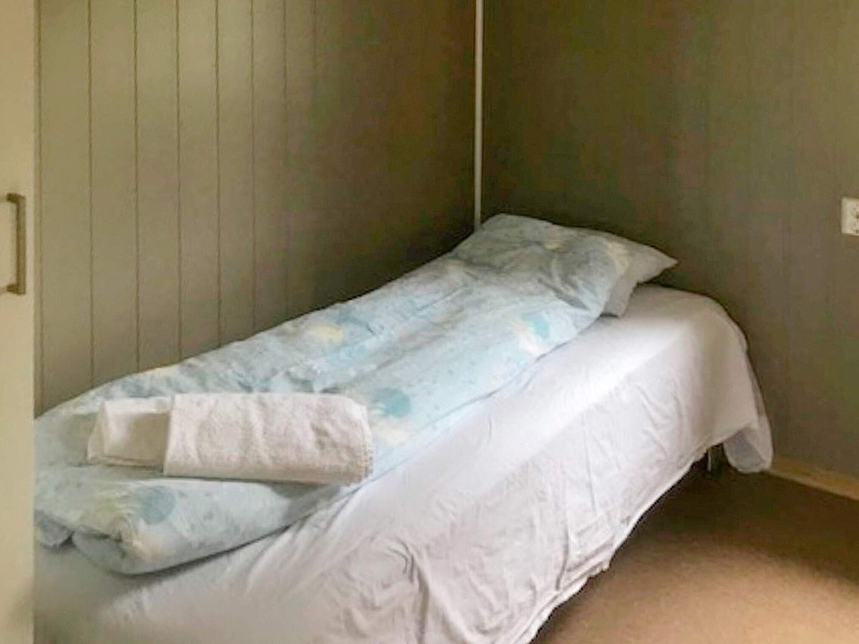 Une petite chambre avec un lit simple, un mur uni et une porte sur un des côtés.
