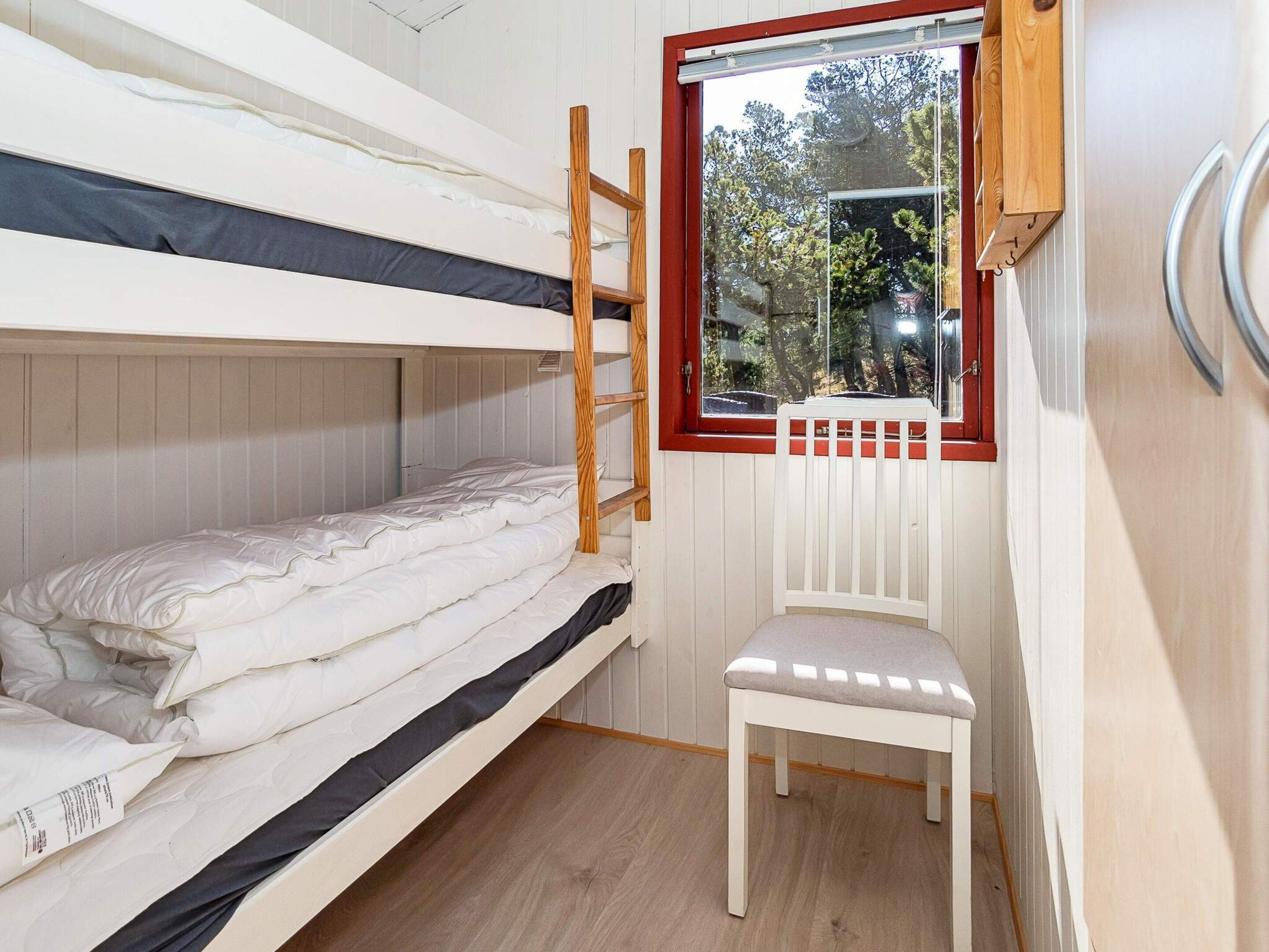Dormitorio con literas, ventana, una silla blanca y escalera de madera.