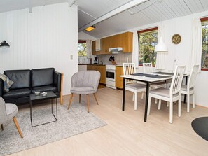 En moderne stue med sofa, spisebord med stole, et køkken og udsigt til det fri.