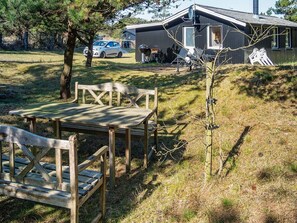 Et træbænk og bordstille står i en græsplæne med et hus i baggrunden.