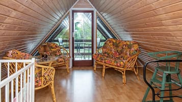 Um quarto de sótão aconchegante, com paredes e chão de madeira, um sofá colorido, uma mesinha e uma cadeira verde.