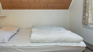 Una cama individual con ropa de cama blanca en una habitación con vigas de madera en el techo y paredes blancas.