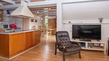 Uma sala de estar ampla com piso de madeira, uma televisão grande e uma poltrona de couro.