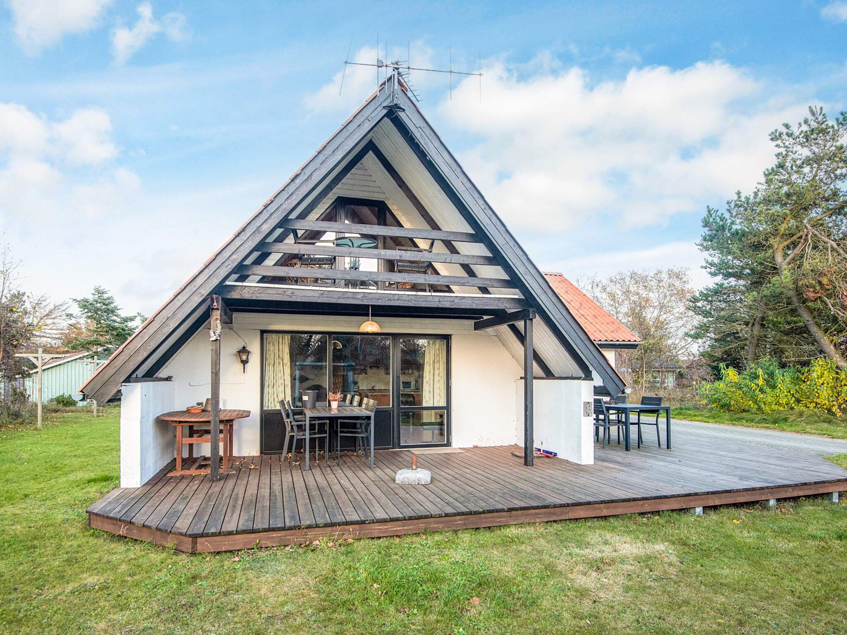 A modern house with a sloped roof, a wooden deck, and a glass door leading to an outdoor dining area.