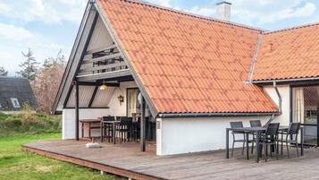 Una casa moderna con techo inclinado, una terraza de madera y un comedor con mobiliario exterior.
