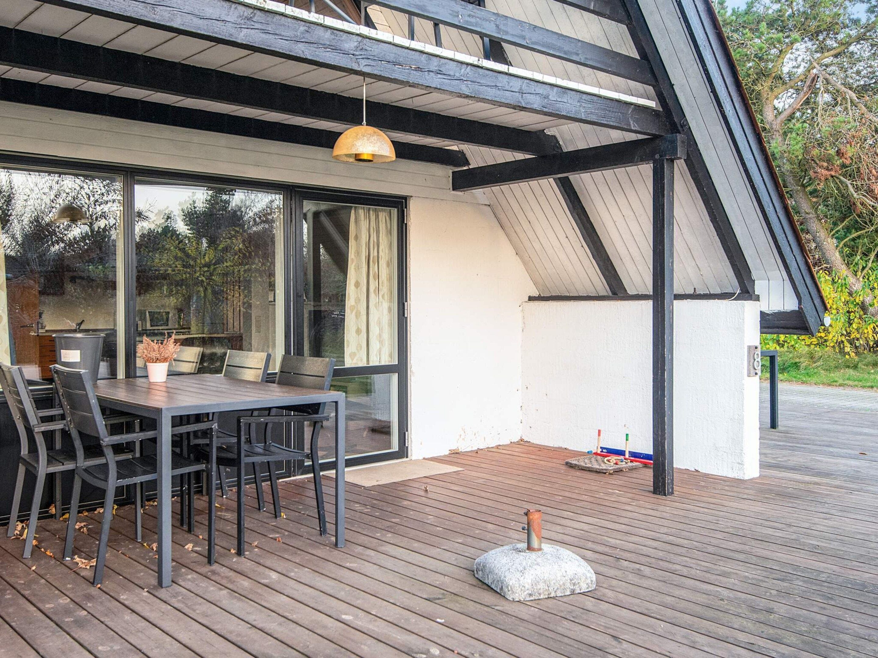 A modern outdoor dining area with a table and chairs, a pergola, and a stone feature on a wooden deck.