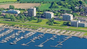 Une vue aérienne d’une marina où sont amarrés de nombreux bateaux, entourée de bâtiments résidentiels et de champs verdoyants.
