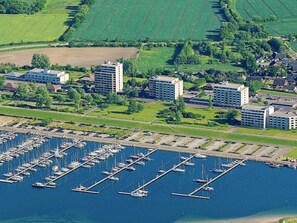 An aerial view of a marina with numerous boats docked, surrounded by residential buildings and green fields.