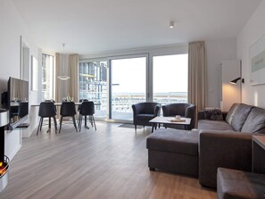 A modern living room with a sofa, armchairs, a dining table, and a TV.