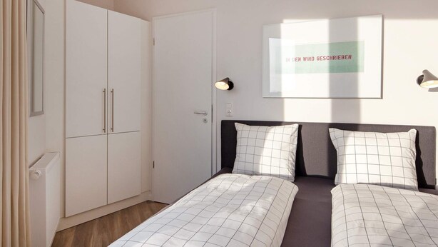 Une chambre avec deux lits, une armoire, une citation encadrée au mur et une lampe de chevet.