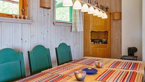 Uma área de refeições com mesa de madeira, jogos americanos listrados, cadeiras verdes e luminárias pendentes.