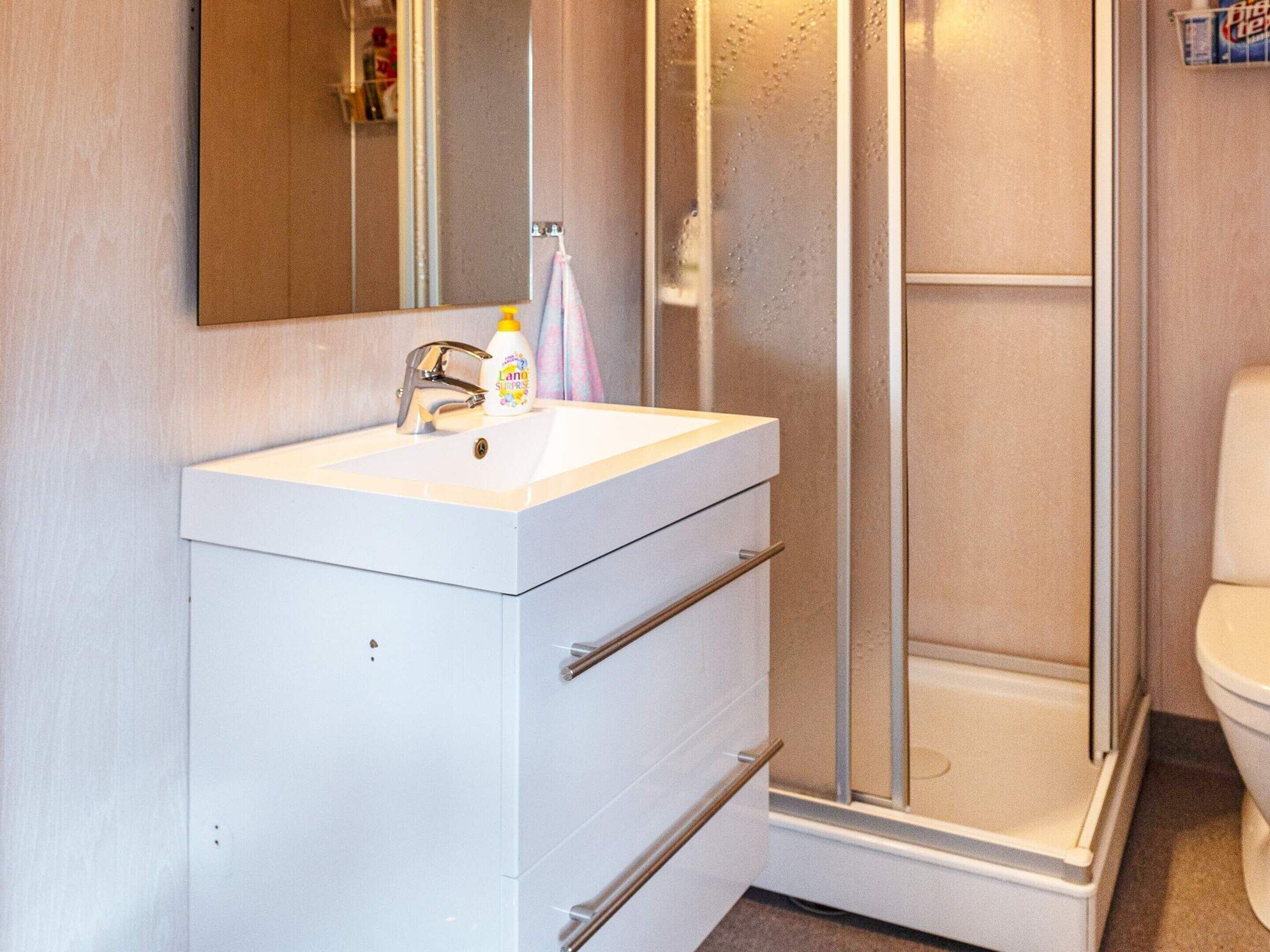 Un bagno con un lavandino bianco, uno specchio e un box doccia.