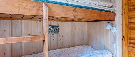 A bunk bed room with wooden walls, a small shelf with books, and a wall-mounted lamp.