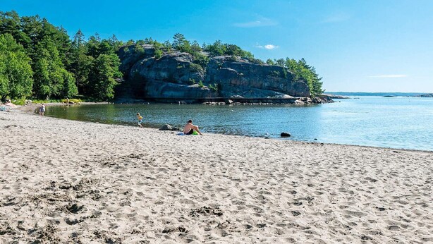 Uma praia arenosa com formações rochosas e árvores ao fundo.