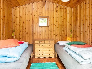 A room with wooden walls, two beds with pillows, a wooden dresser, and a small window. - 6 Person Holiday Home in Kolind (Kolind)