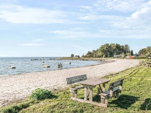 A beach with wooden benches and picnic tables, a sandy shore, and a pier with boats. - 6 Person Holiday Home in Kolind (Kolind)