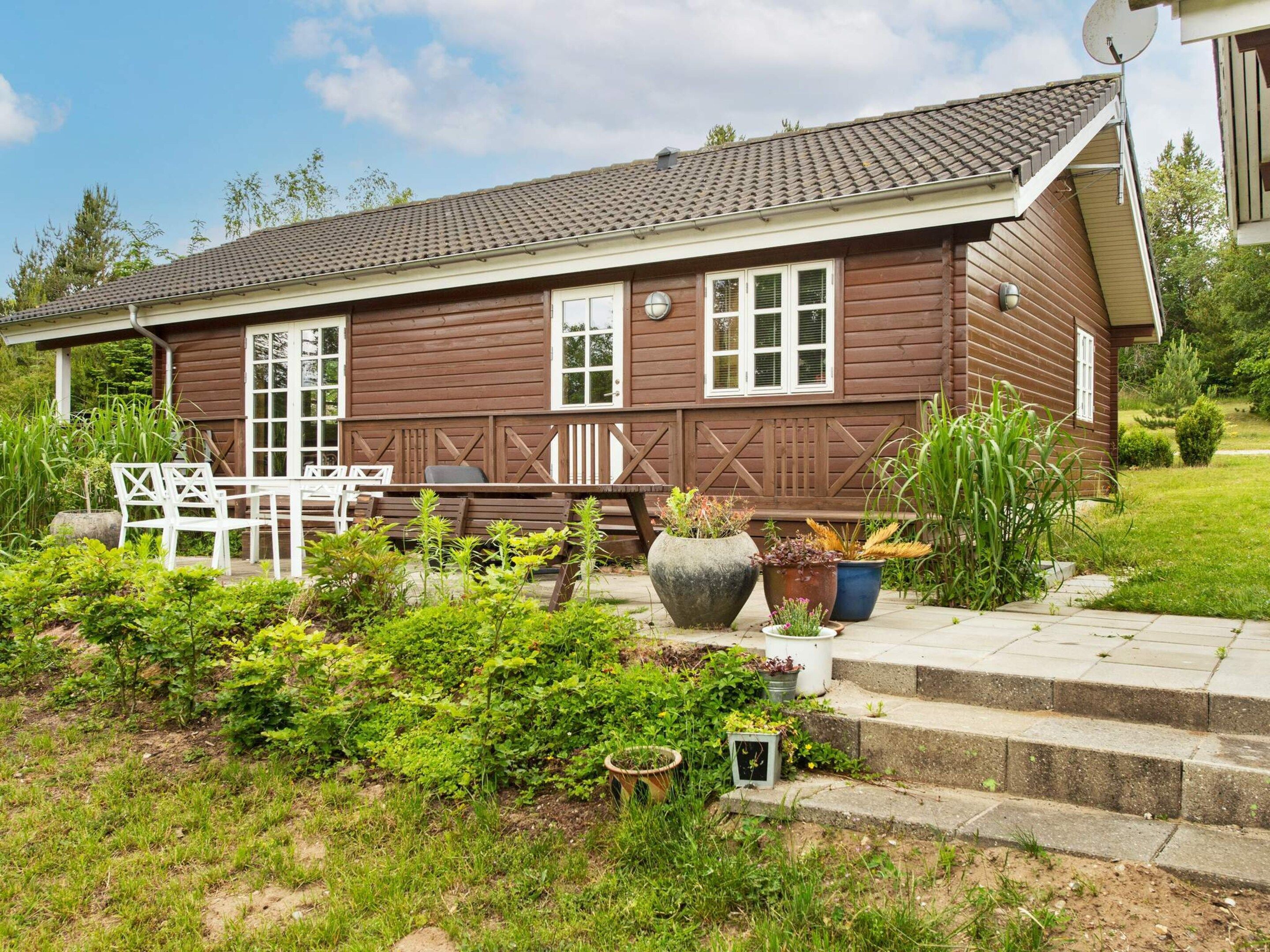 Une maison en bois avec un porche, des meubles d’extérieur blancs et des plantes en pot.
