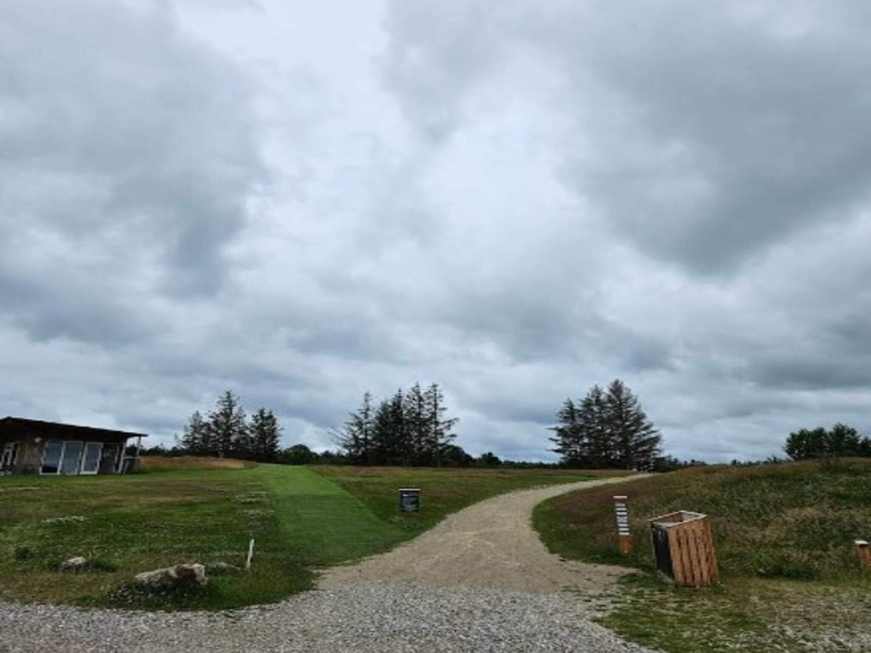 A gravel path leading to a building with a sloped roof, surrounded by grassy fields and trees.
