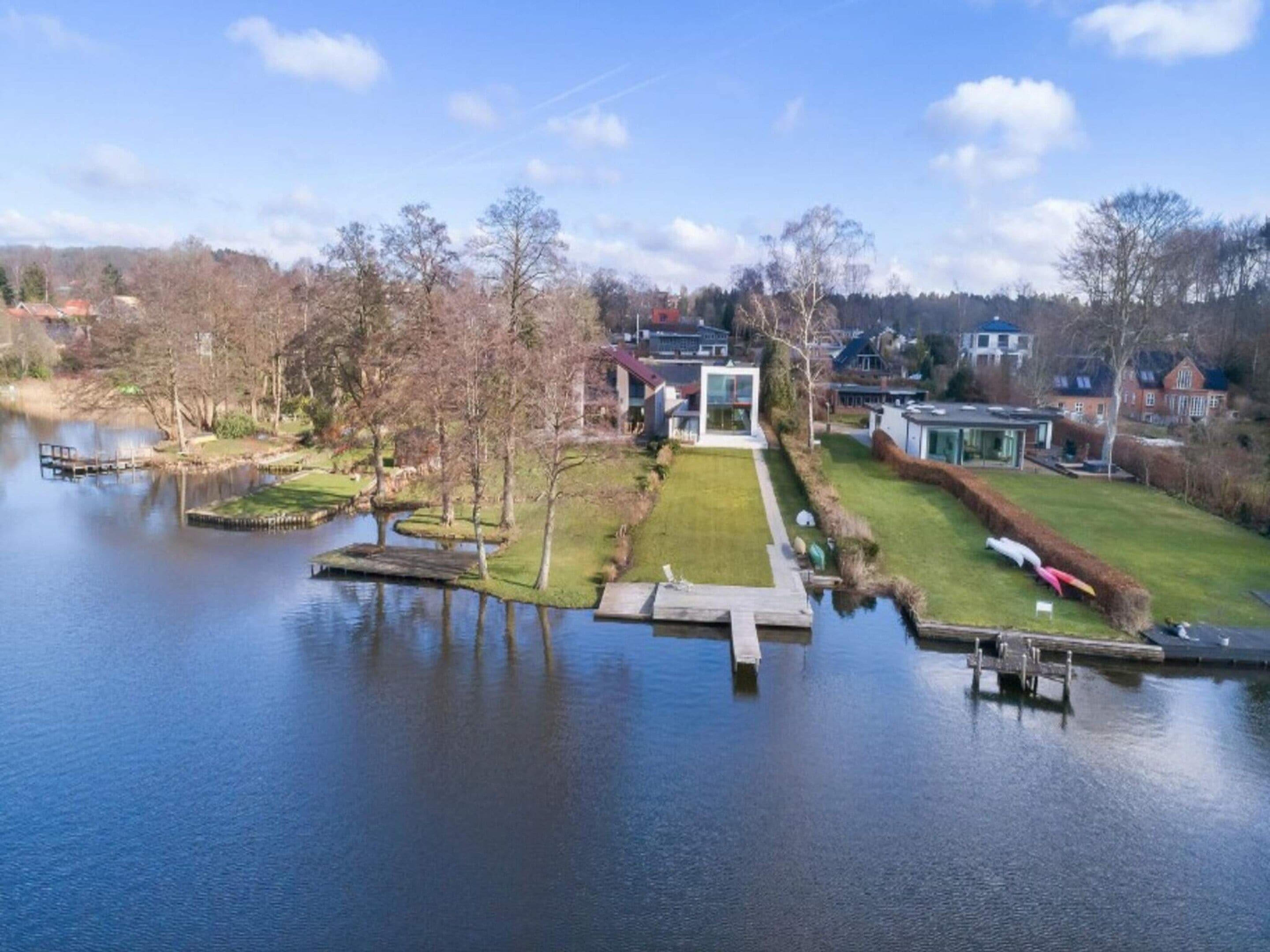 A lakeside property with a dock, a grassy lawn, and a modern house with a glass facade.