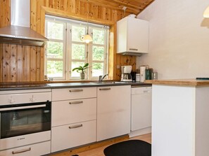A kitchen with wooden paneling, a Bosch oven, a coffee maker, and a window with a view of greenery. - 6 Person Holiday Home in Kolind (Kolind)