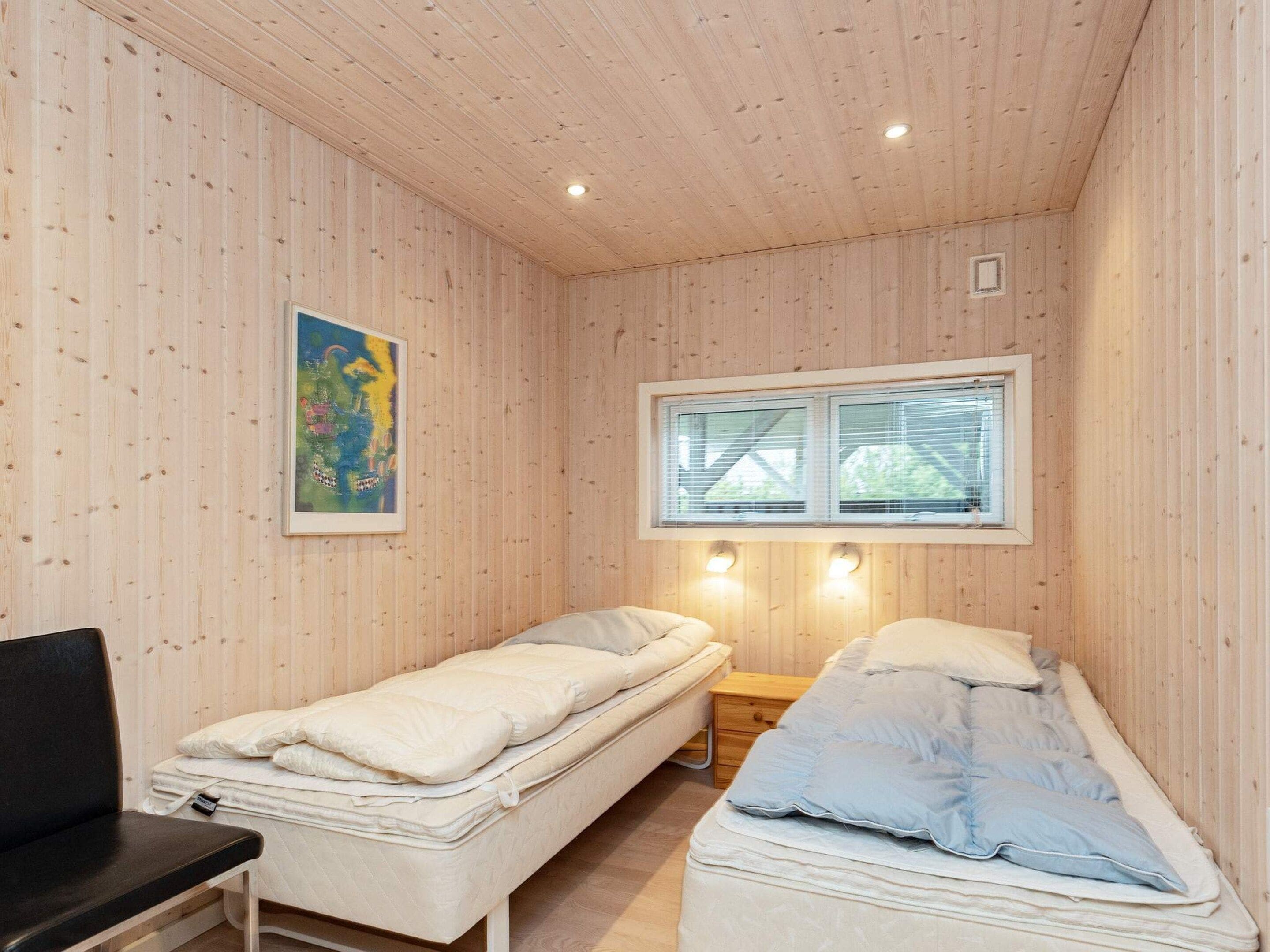 A room with two single beds, a desk, a chair, a window with blinds, and a painting on the wall.