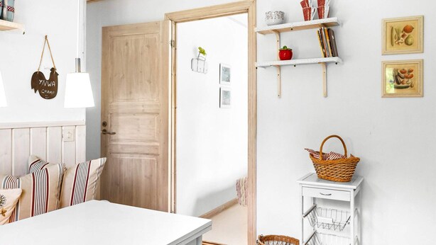 A room with a white table, striped cushions, a wooden door, and shelves with kitchen items. - 8 Person Holiday Home in Skanes Fagerhult (Skånes Fagerhult)