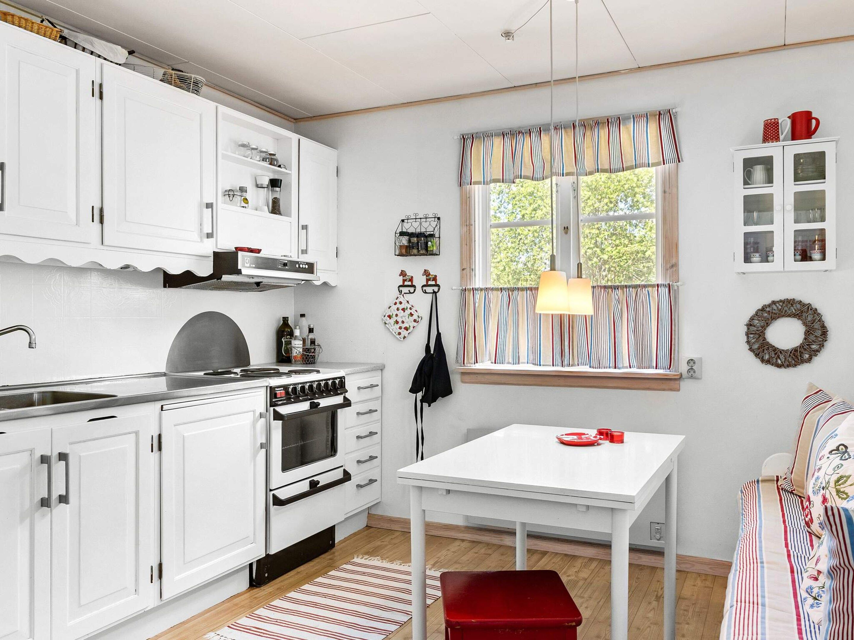 Una cocina con armarios blancos, estufa, lavamanos y ventana con cortinas a rayas.