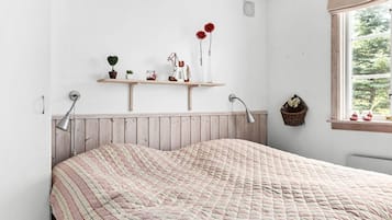 A bedroom with a bed, bedside lamps, a window with a view, and a shelf with decorative items.