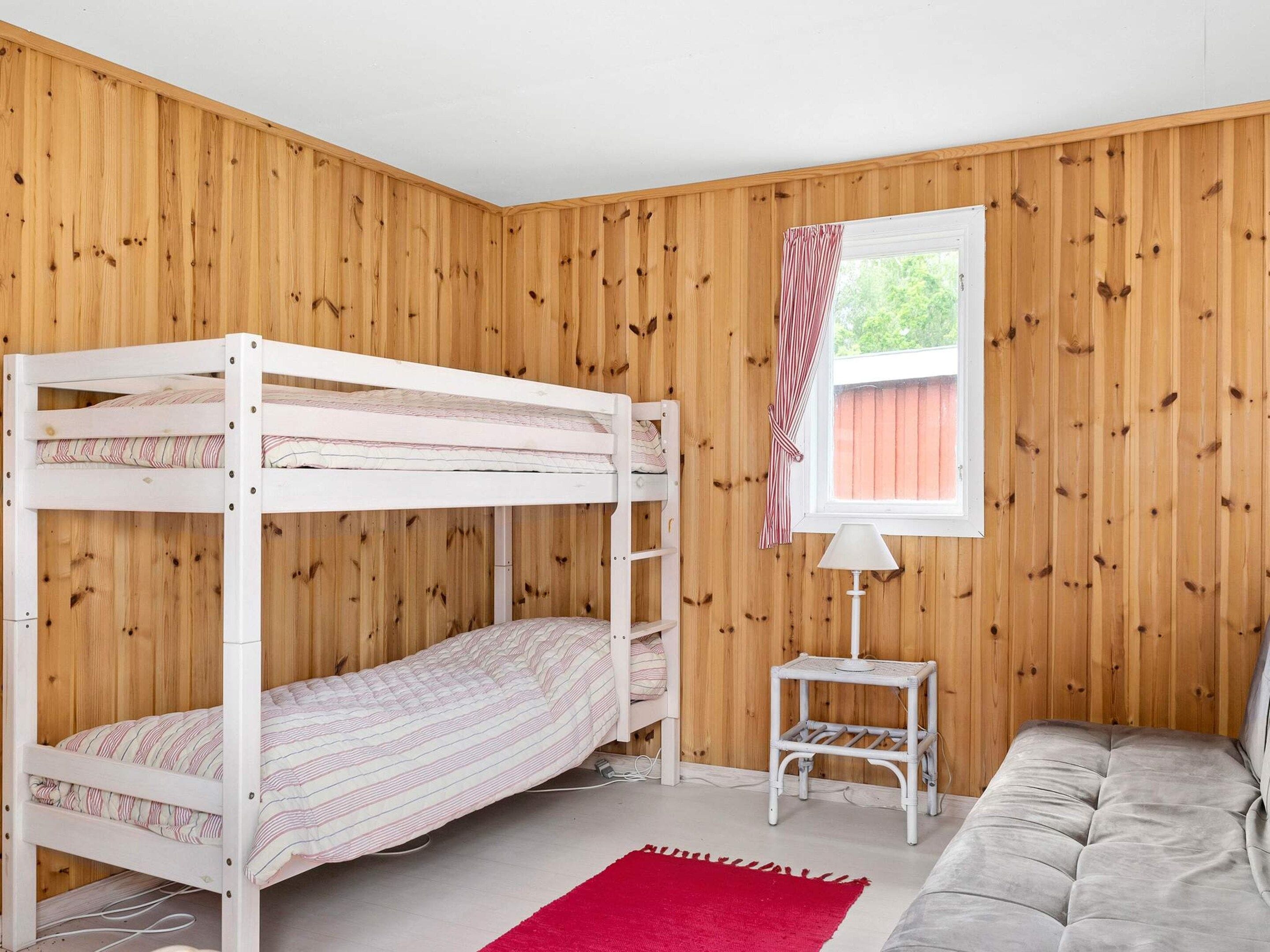 Habitació amb parets de fusta, un llit superposat, una taula petita, un sofà i una finestra amb cortines.