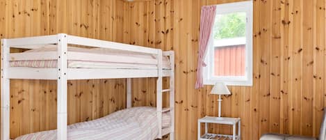 Habitació amb parets de fusta, un llit superposat, una taula petita, un sofà i una finestra amb cortines.