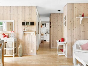 A room with wooden panel walls, a white sofa, a dining table, and a kitchen area in the background. - 8 Person Holiday Home in Skanes Fagerhult (Skånes Fagerhult)
