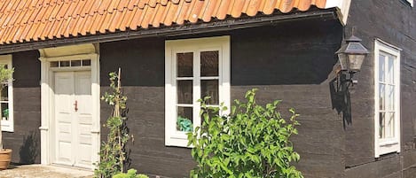 A house with a dark facade, a tiled roof, a white door, and a window with a white frame.
