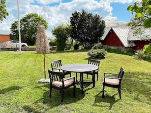 A grassy outdoor area with a round table and four chairs, a thatched umbrella, and a red building in the background. - 6 Person Holiday Home in Kopingsvik (Kopingsvik)