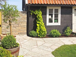 A house with a stone wall, a window with a plant inside, and a garden with various plants. - 6 Person Holiday Home in Kopingsvik (Kopingsvik)