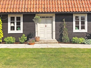 A house with a red-tiled roof, a white door, and a small front garden with potted plants. - 6 Person Holiday Home in Kopingsvik (Kopingsvik)