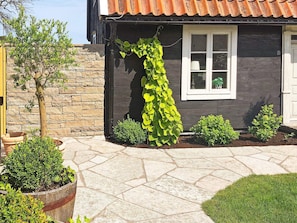 A house with a stone wall, a window with a white frame, and a garden with various plants. - 6 Person Holiday Home in Kopingsvik (Kopingsvik)
