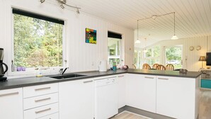 Une cuisine moderne avec des meubles blancs, un plan de travail noir et un lave-vaisselle. Une fenêtre offre une vue sur la verdure à l’extérieur.