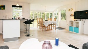 Une cuisine moderne avec des meubles blancs, un coin repas avec des chaises en bois et un téléviseur fixé au mur.