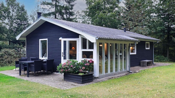 Une maison moderne dotée d’un patio couvert, d’un coin repas avec mobilier d’extérieur et d’un jardin fleuri.