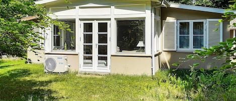A small, single-story building with a sloped roof, large windows, and a visible air conditioning unit.