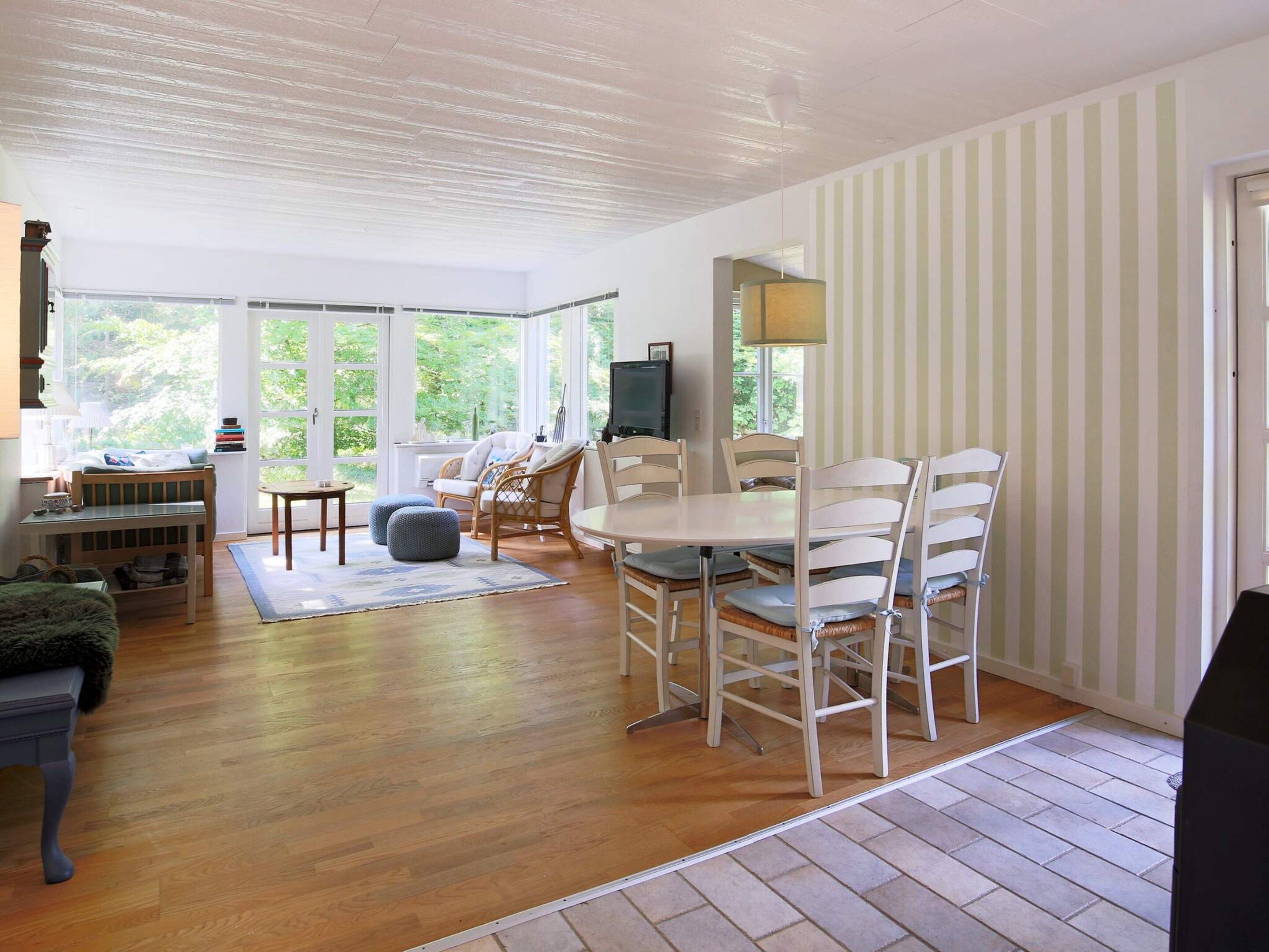 A spacious room with a dining table and chairs, a television, and large windows providing natural light.