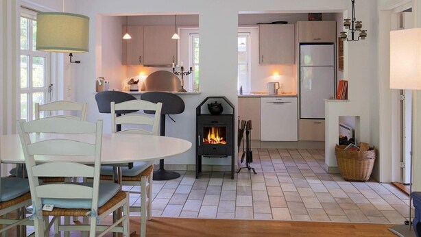 Una cocina moderna con una isla central, un comedor con sillas blancas y una estufa de leña.