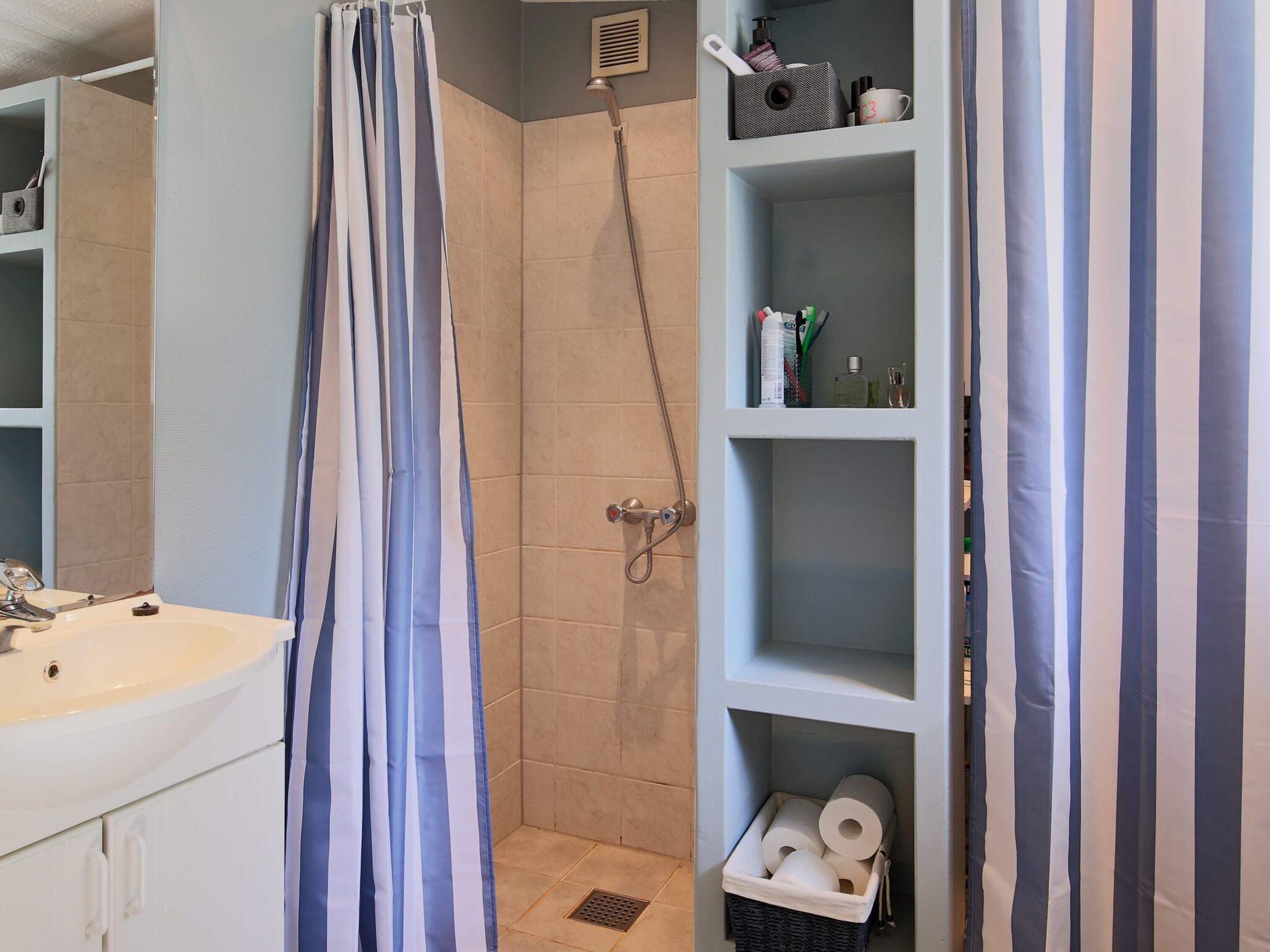 Ein Badezimmer mit Dusche, Waschbecken und Regalen mit Pflegeprodukten.