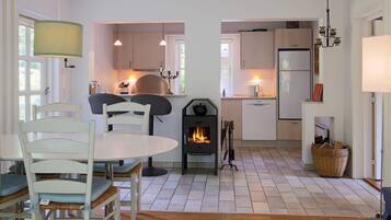 A modern kitchen with white cabinets, a dining area with white chairs, a wood-burning stove, and a chandelier.