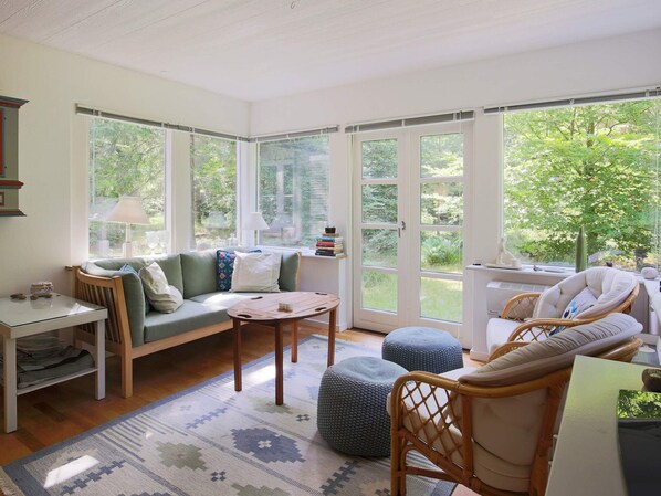 Una habitación acogedora con sofá, mesa, silla, ventanas amplias y vistas al exterior.