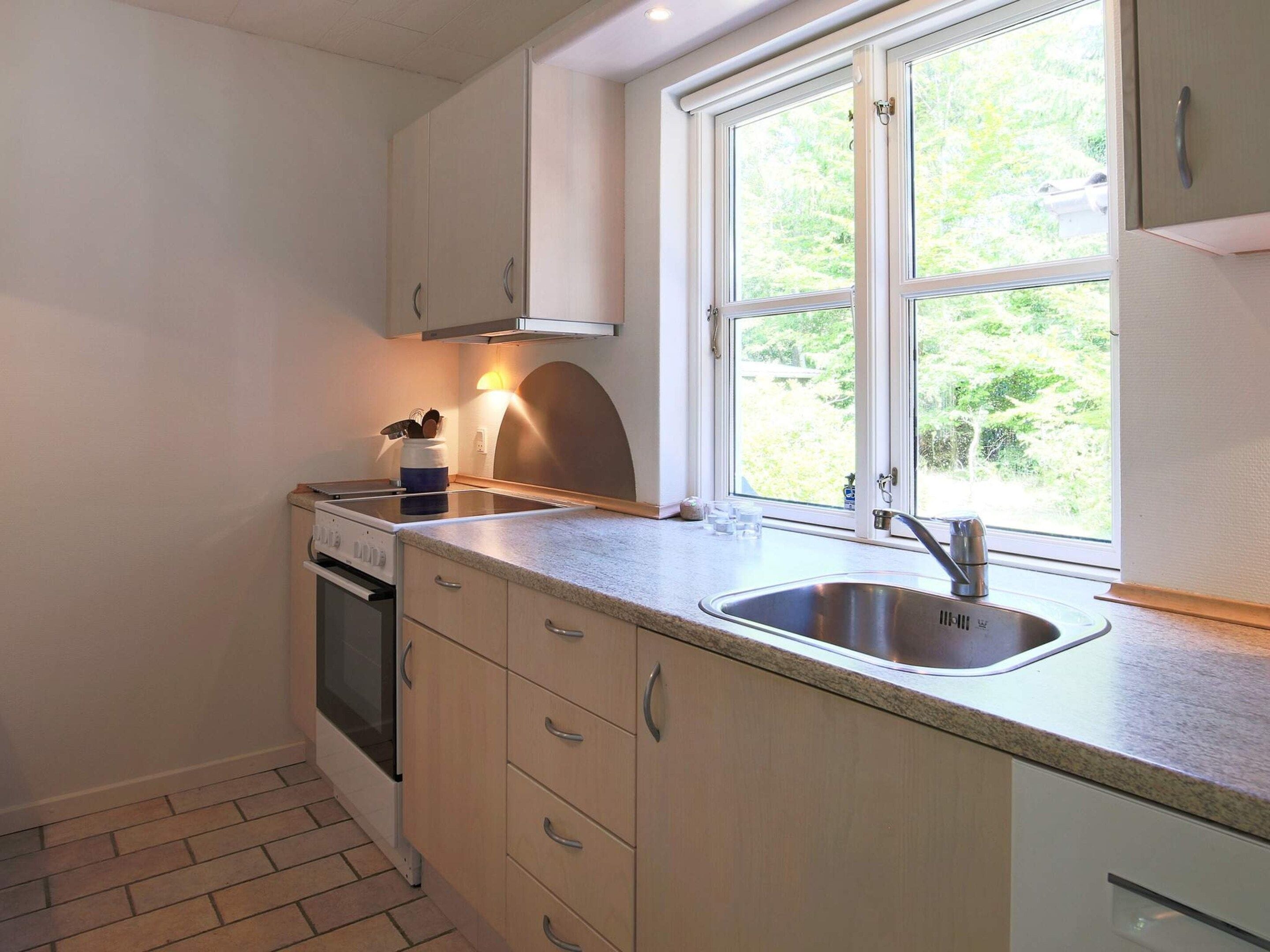 A kitchen with a window, a sink, cabinets, and a stove.